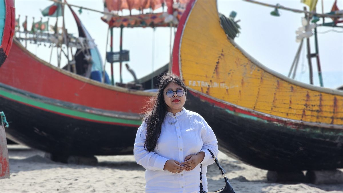 A woman in white standing in front of colourful fishing boats on the beach